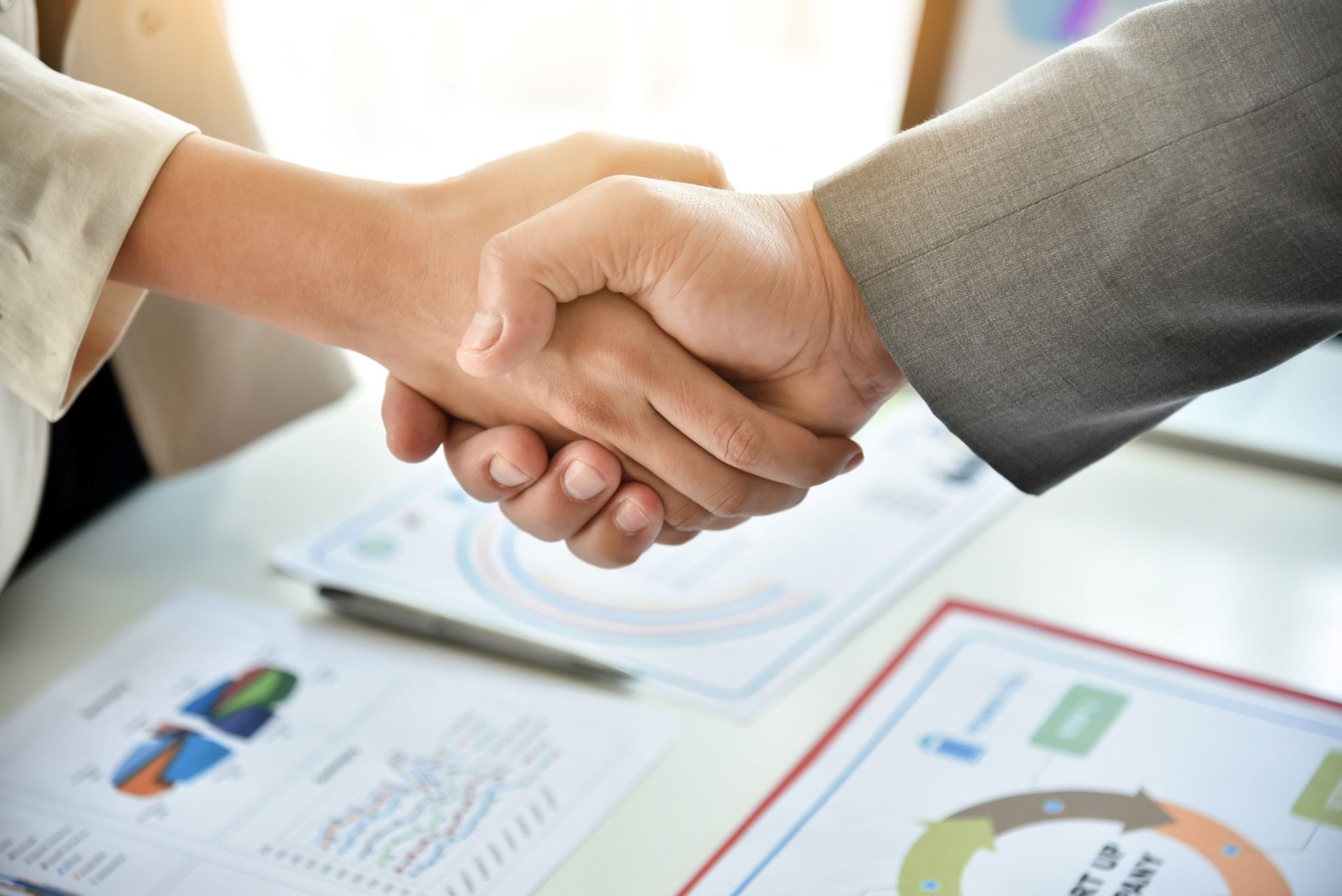 Two people shaking hands over a desk with documents; business agreement.
