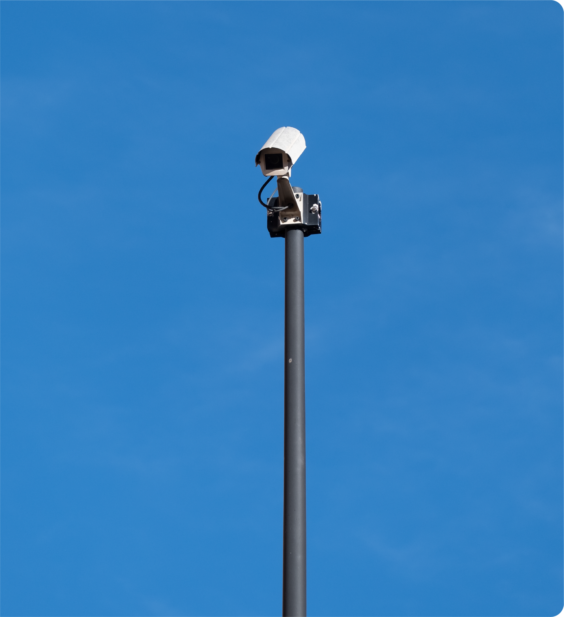 A security camera on top of a pole with a blue sky in the background