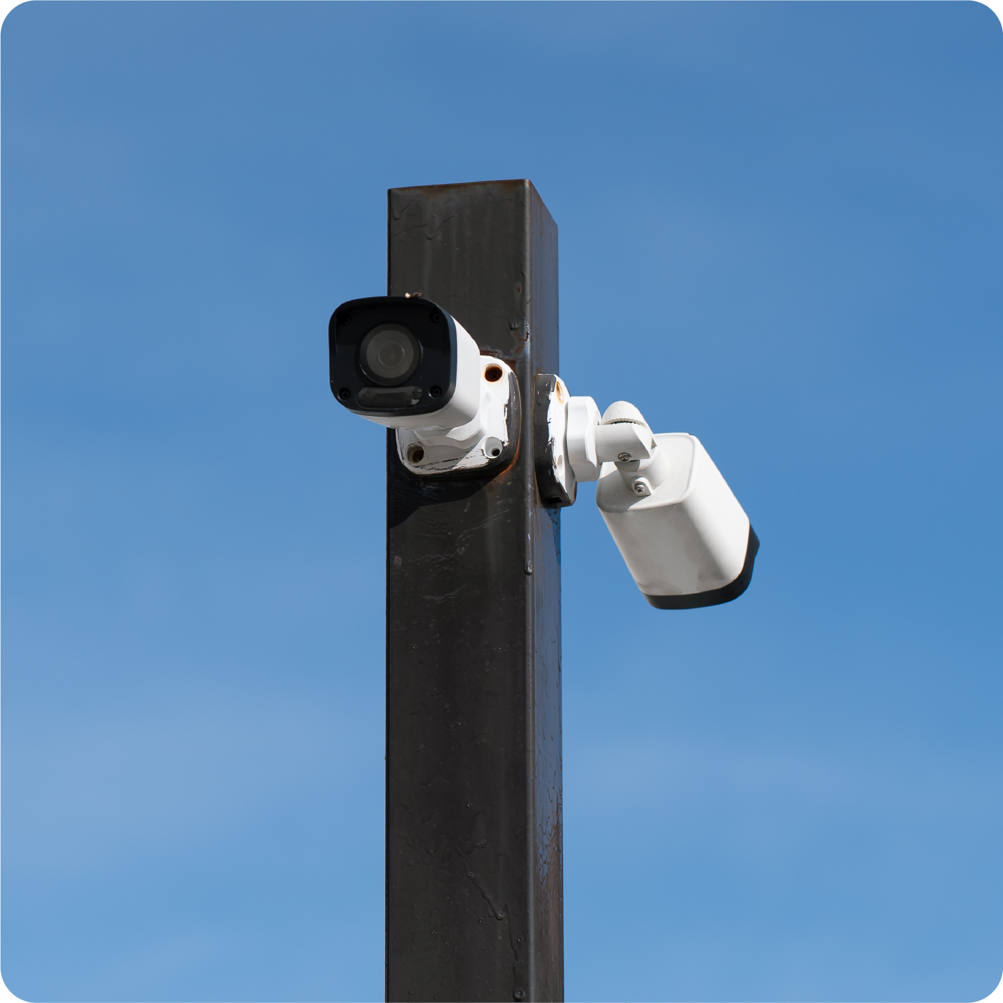A security camera mounted to a pole with a blue sky in the background.
