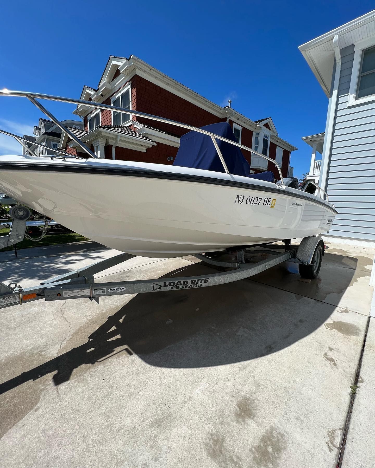 A boat on a trailer is parked in front of a house.