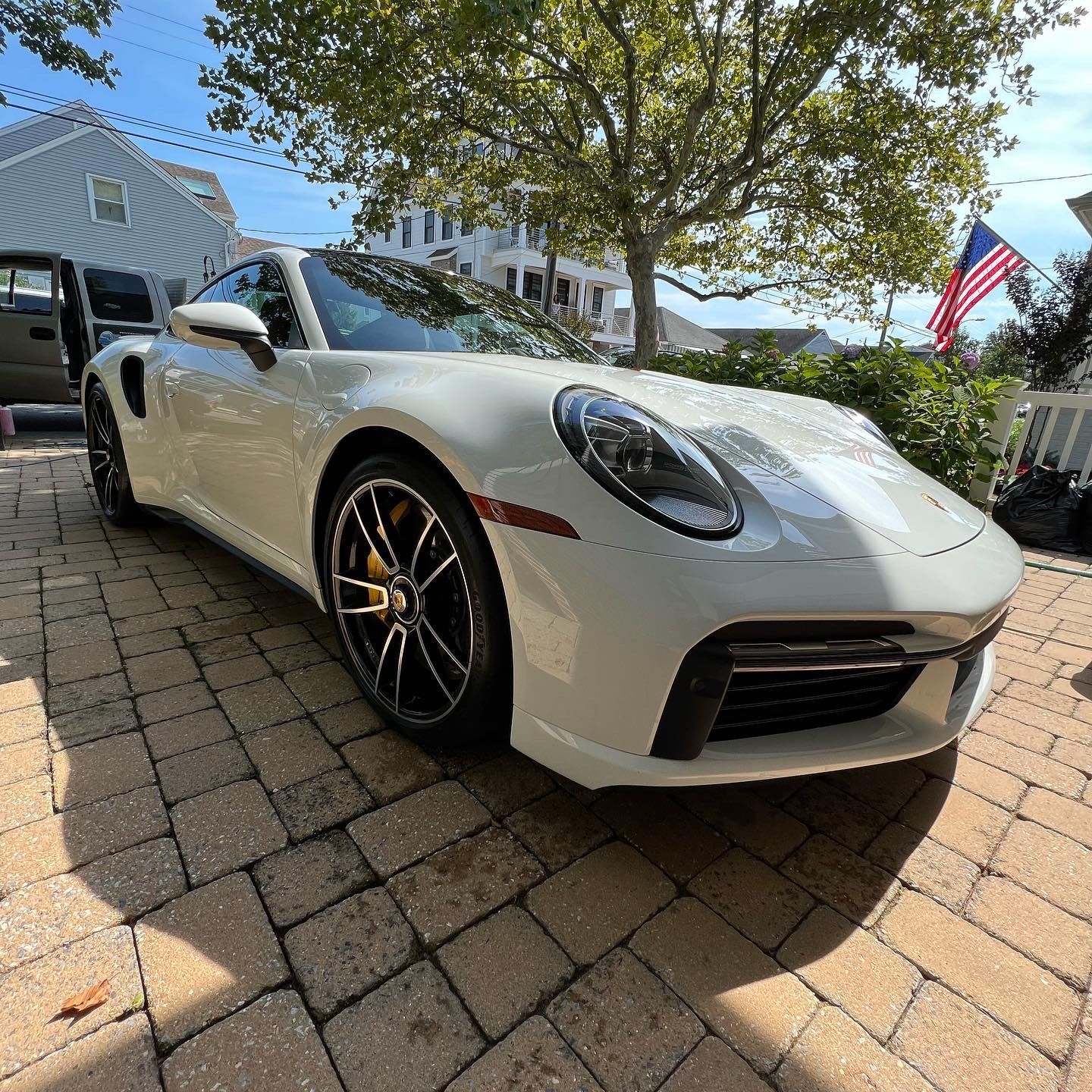 A white porsche 911 turbo s is parked on a brick driveway.