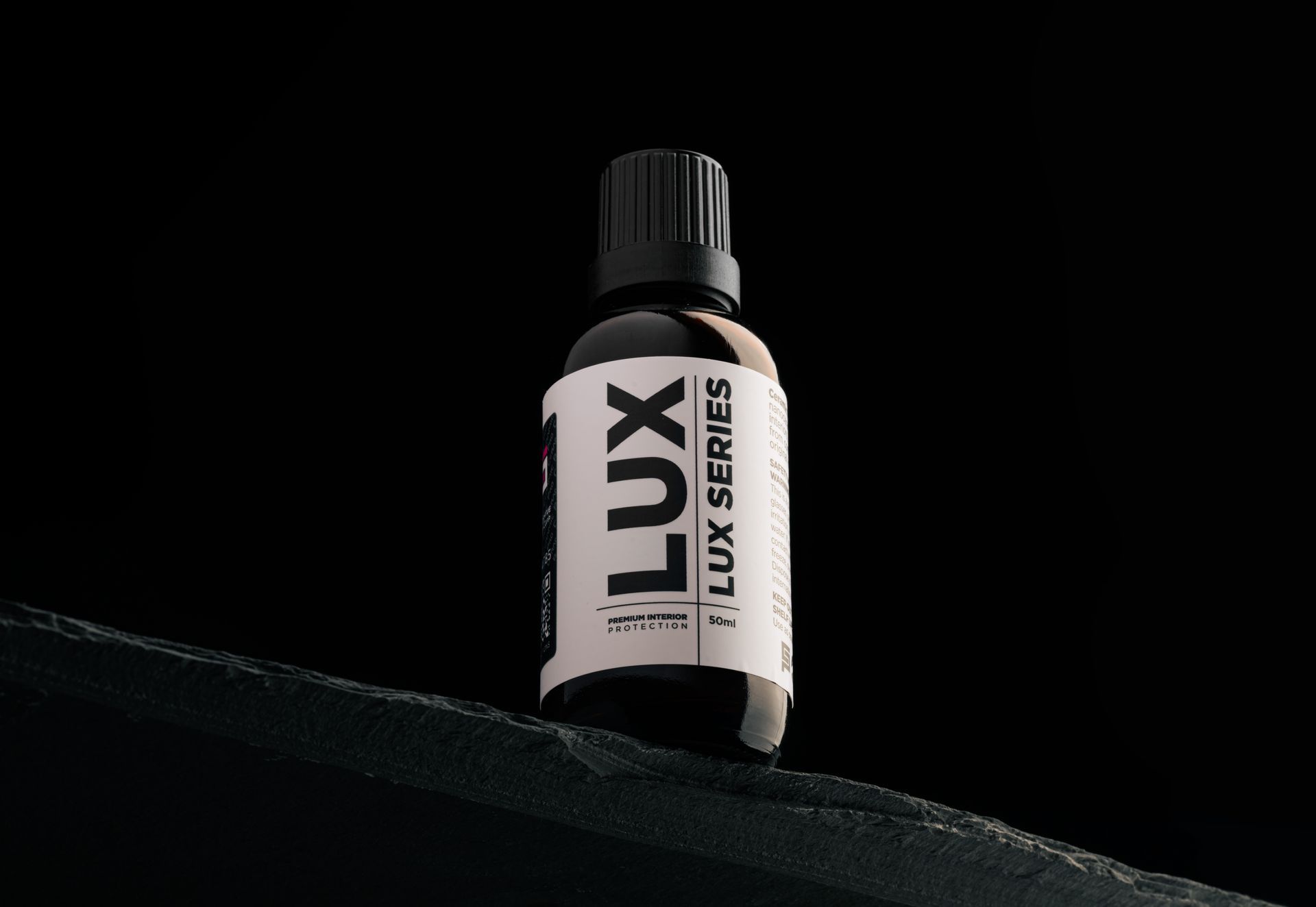 A bottle of lux series essential oil is sitting on a black surface.