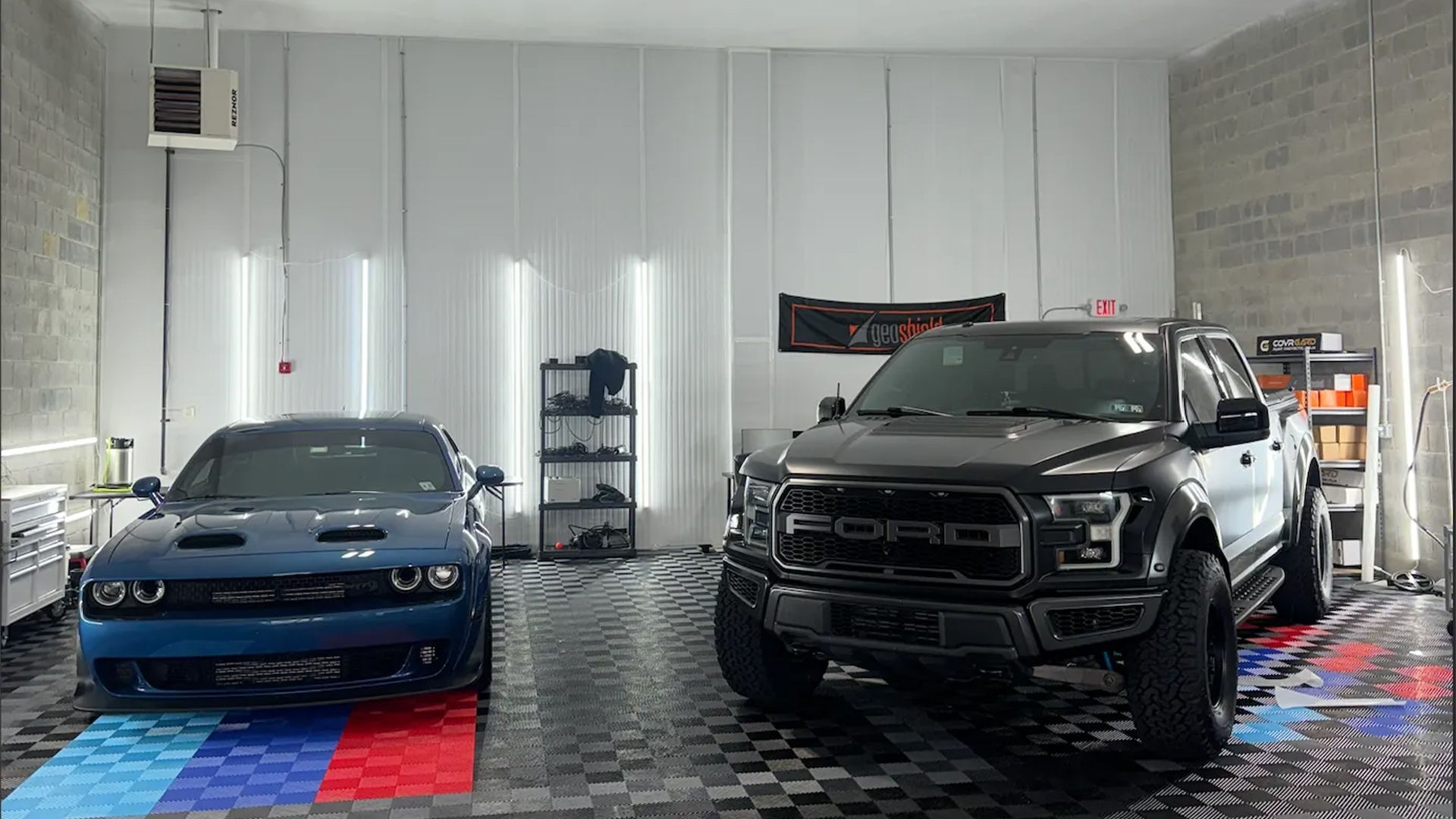 A Dodge Challenger and Ford Raptor truck parked in a well-lit garage with colorful flooring.