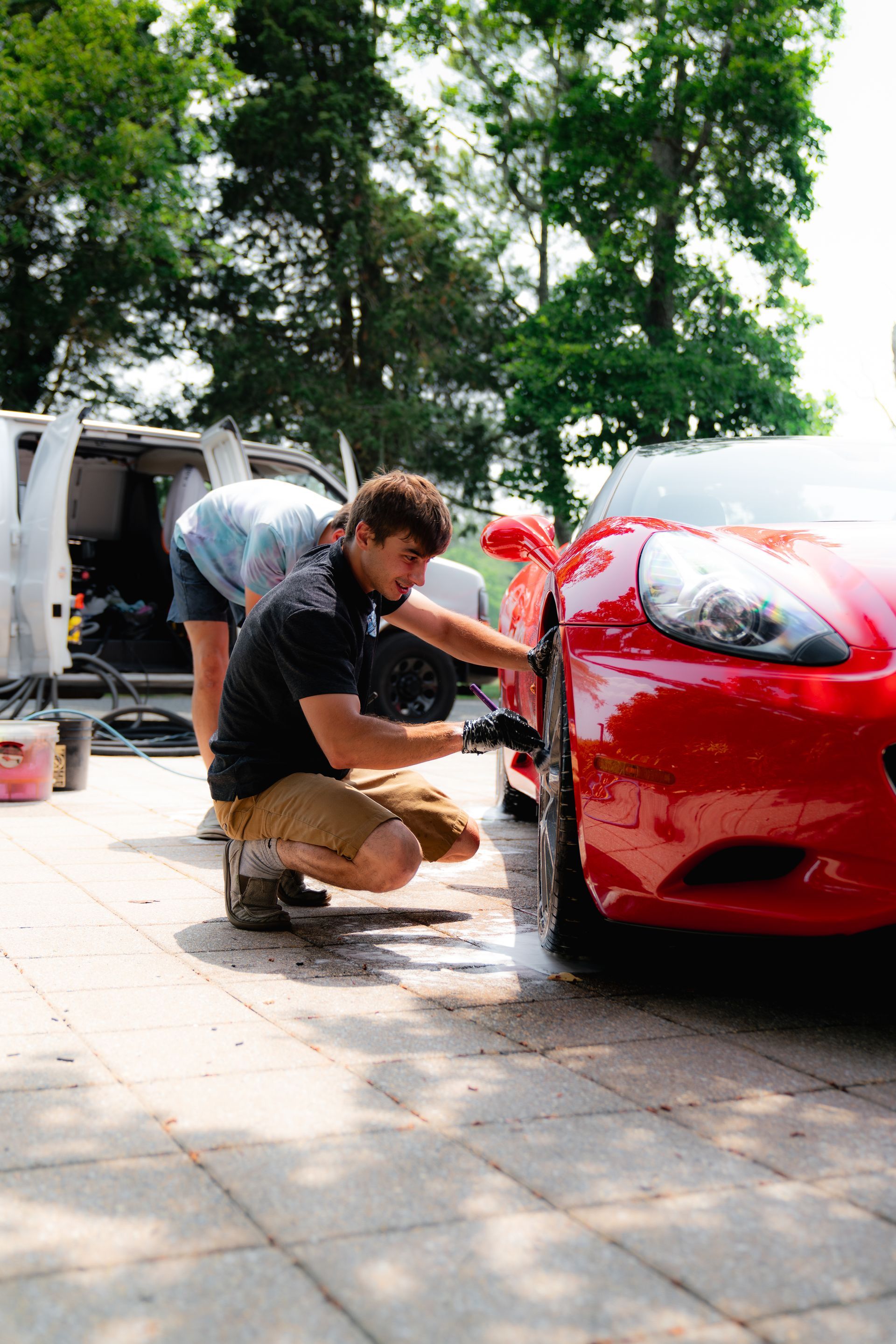 A man is kneeling down to wash a red sports car.