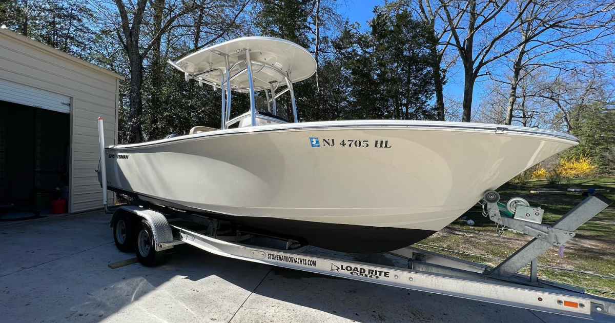 A white boat is on a trailer in front of a garage.