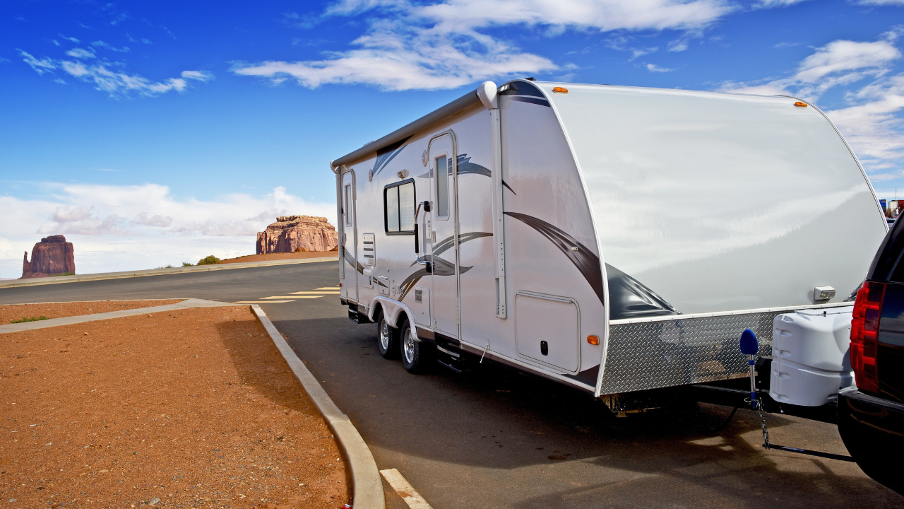 RV parked on a paved road with red rock formations in the background on a sunny day.