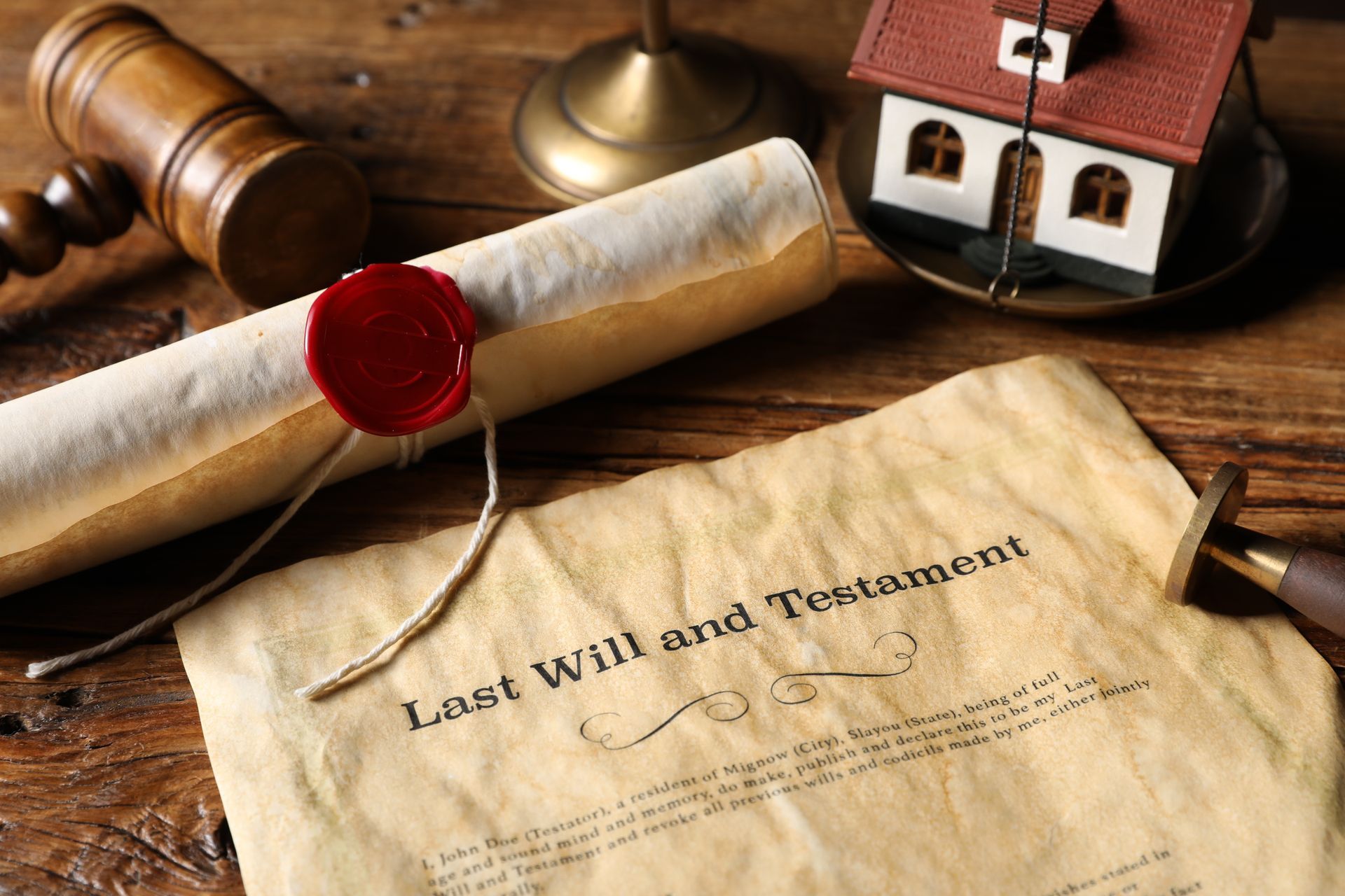 Last will and testament displayed with a sealed scroll, gavel, and model house on a desk.