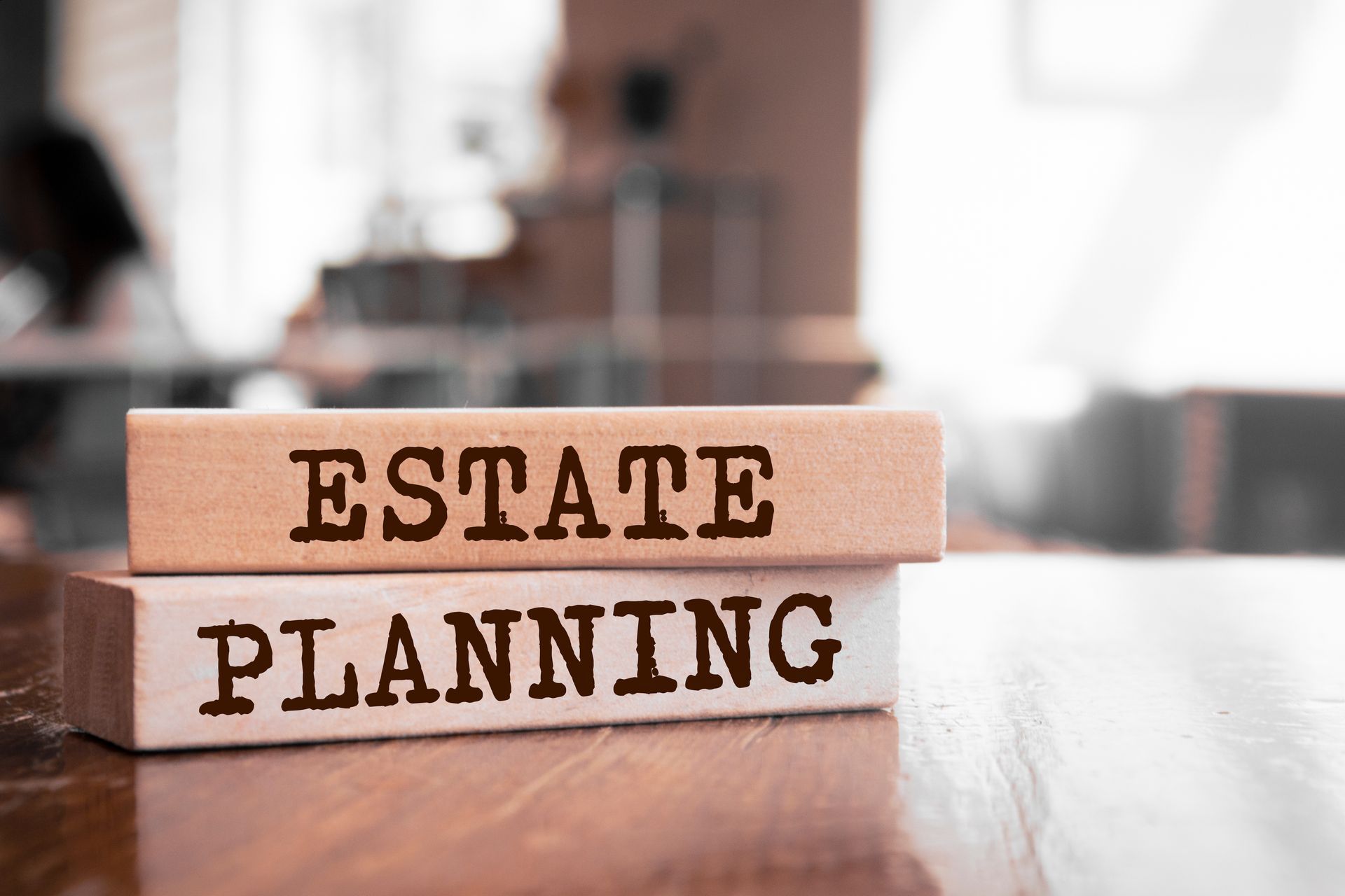 Wooden blocks labeled “Estate Planning” stacked on a desk in an office setting. Wooden blocks labeled “Estate Planning” stacked on a desk in an office setting.