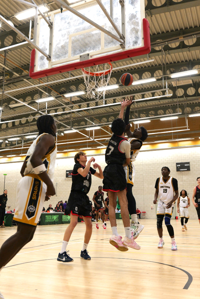 Basketball players jump for a layup beneath a red rim in an indoor gym