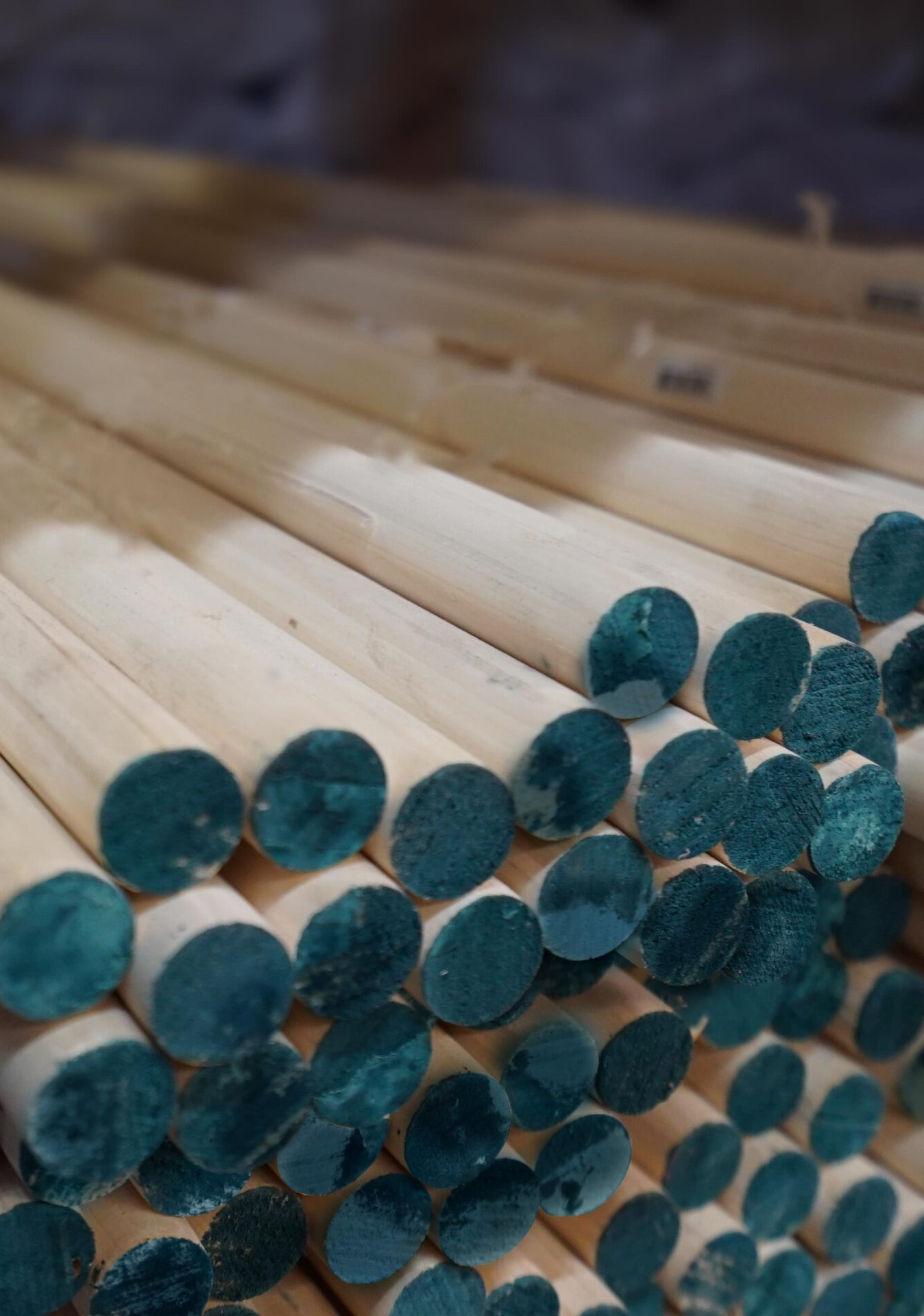 A pile of wooden sticks with blue ends stacked on top of each other.