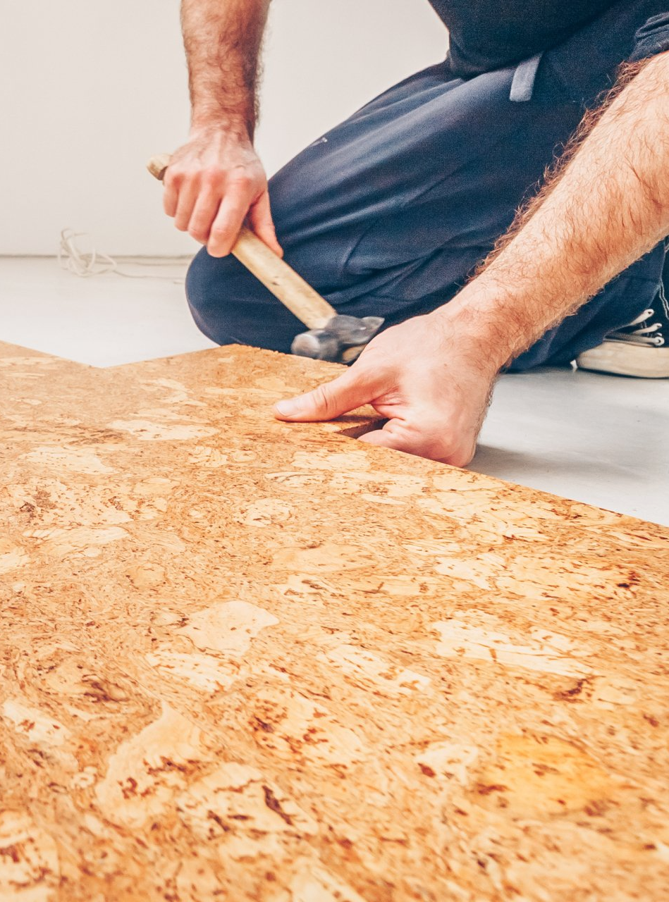A man is kneeling down and hammering a piece of cork flooring.