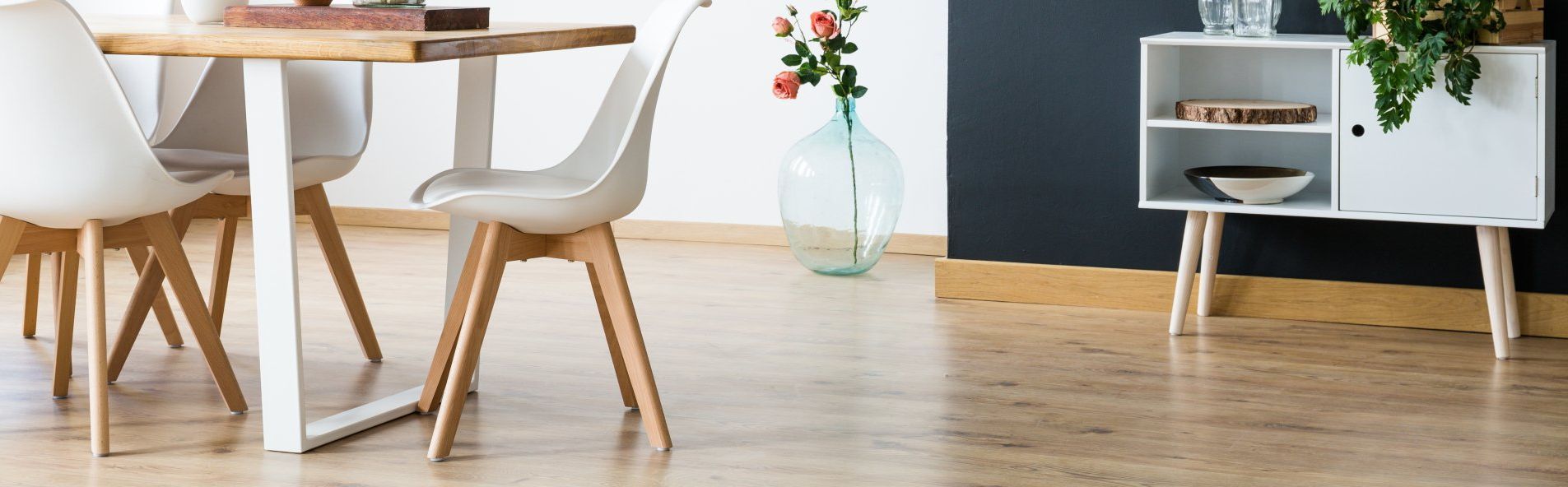 Salle à manger avec une table en bois et des chaises blanches, ainsi qu'une armoire et un vase avec des fleurs.