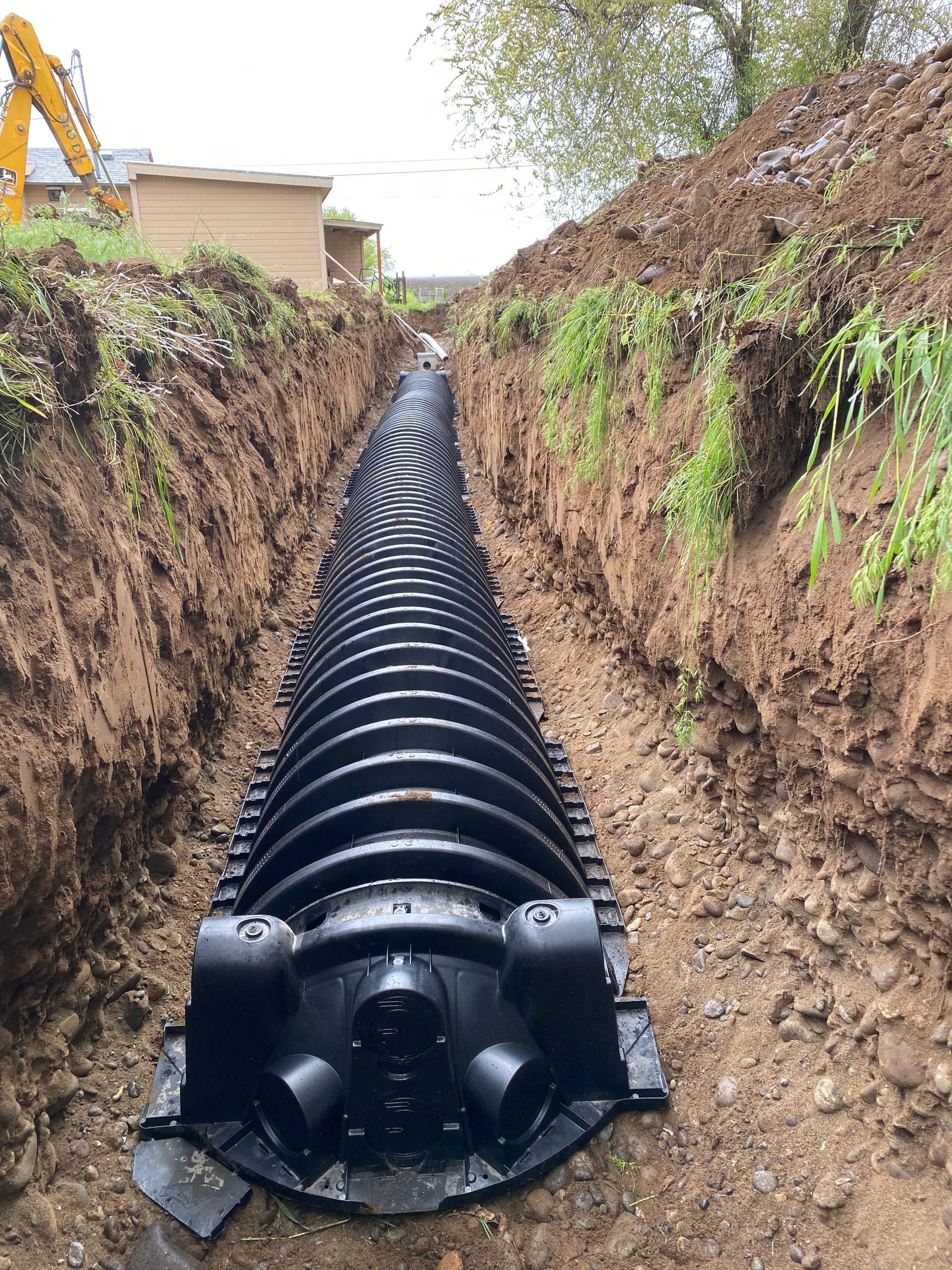 A large black pipe is being installed in a trench.