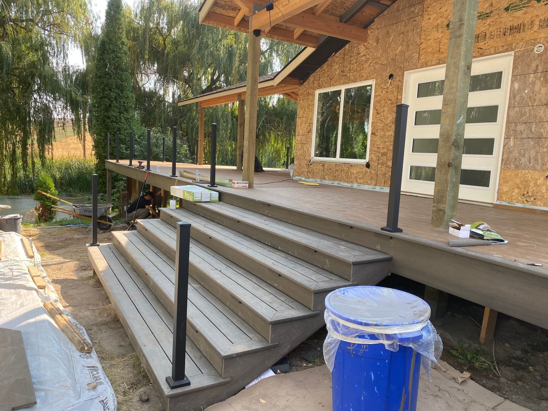 A blue bucket is sitting on the ground in front of a wooden deck.