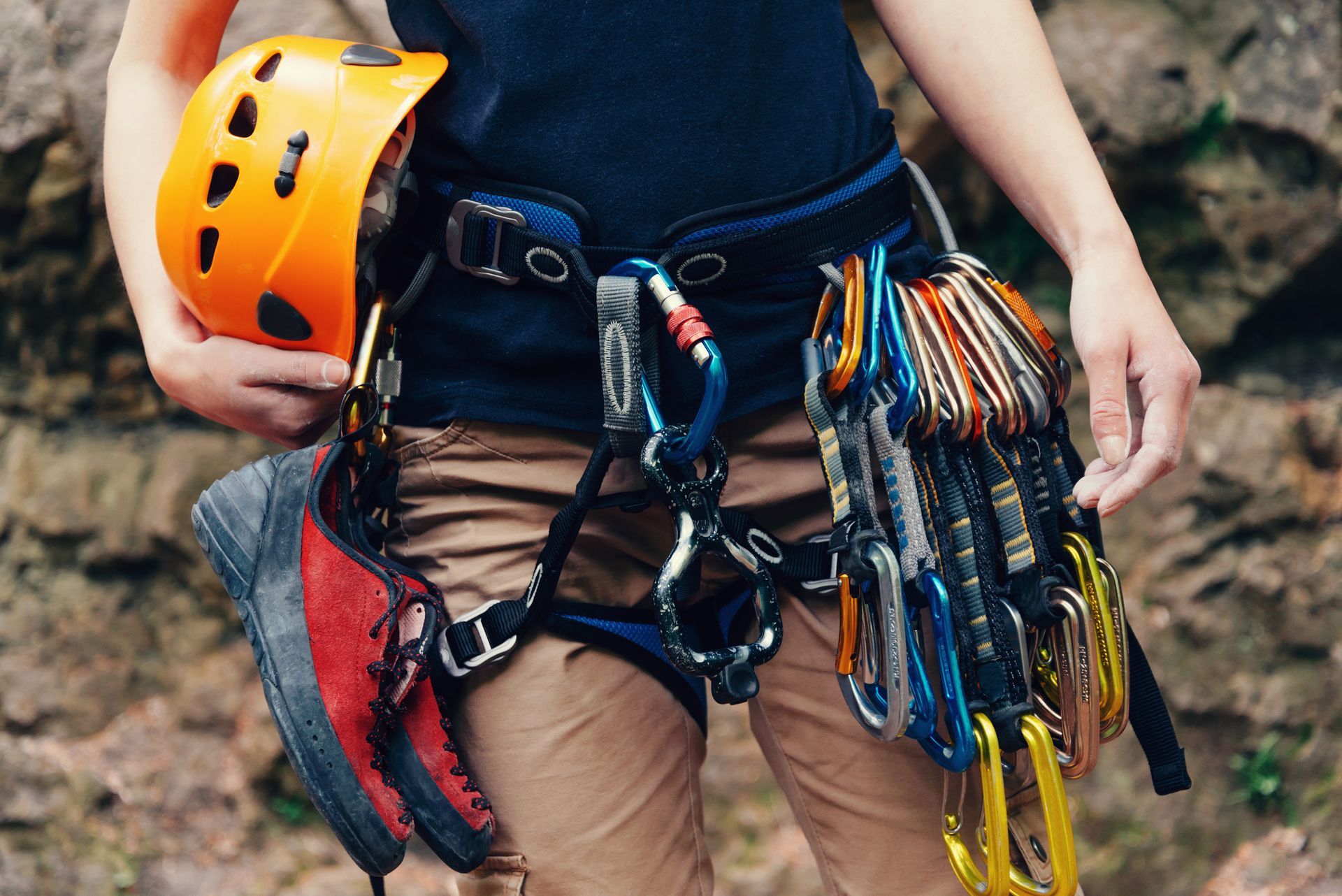 A person is holding a helmet and a pair of climbing shoes.