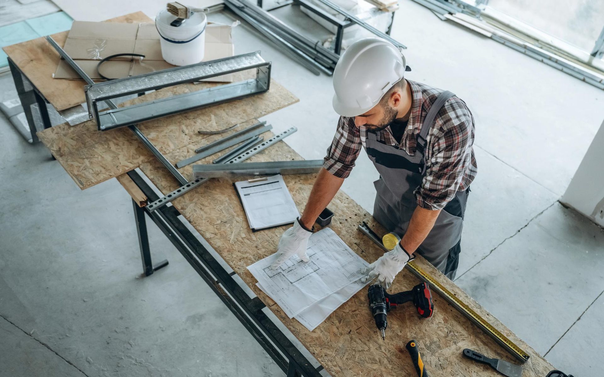 Construction worker in hard hat reviewing blueprints at a workbench in a construction site.