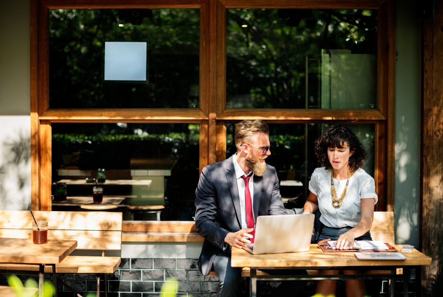 Man and woman working on laptop at outdoor cafe table.