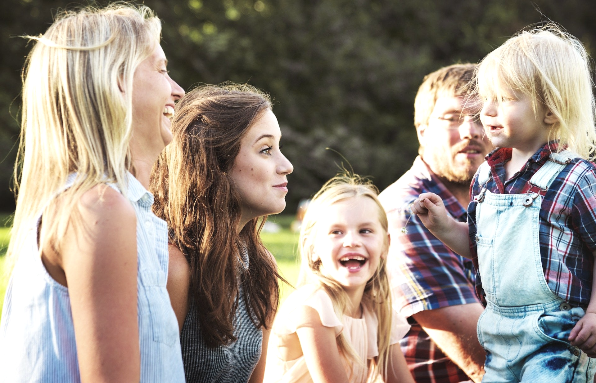 Family smiling and laughing outdoors. A young child gestures while others listen.