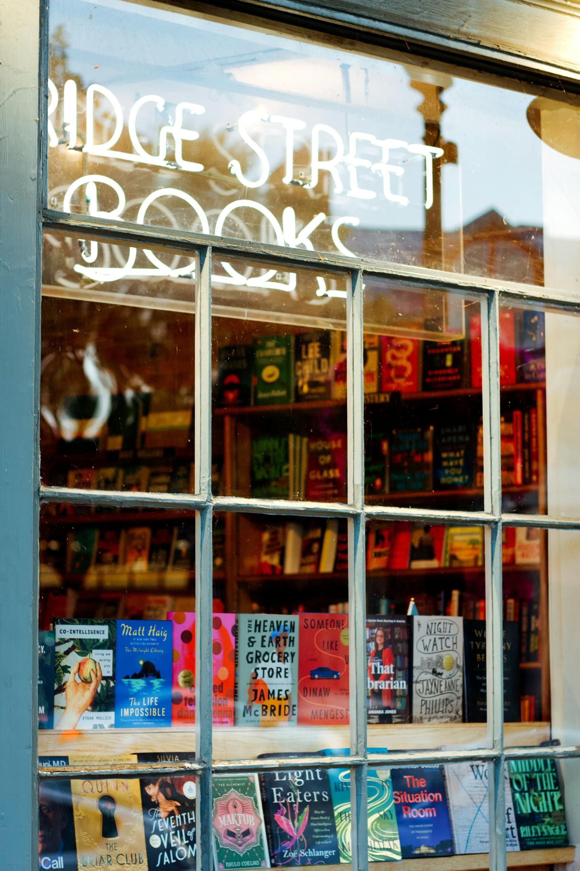 Bridge Street Books storefront window displaying colorful book covers. Neon sign glows above.