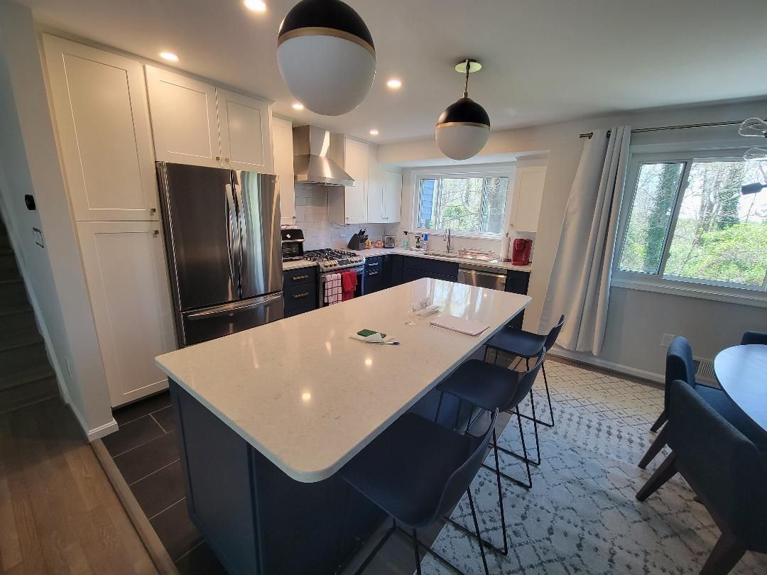 A kitchen with white cabinets , stainless steel appliances , and a large island with stools.