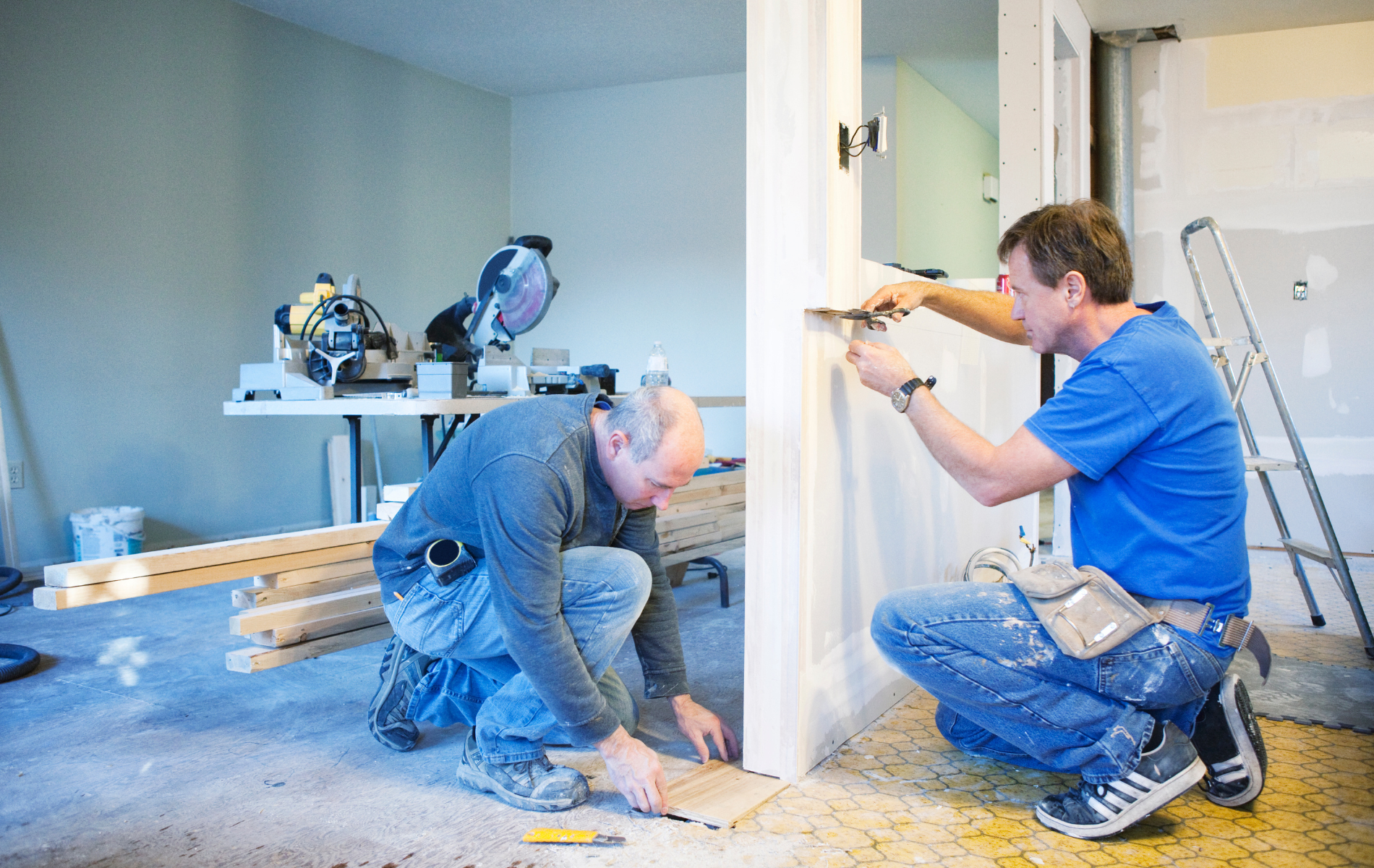 Two men are working on a wall in a room.