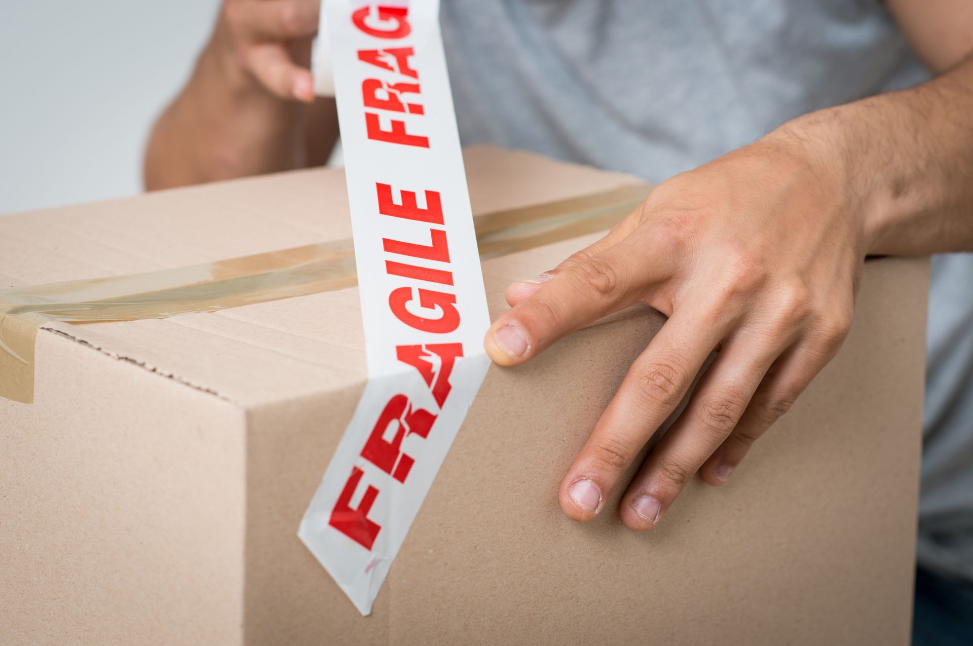 une personne met du ruban adhésif fragile sur une boîte en carton.