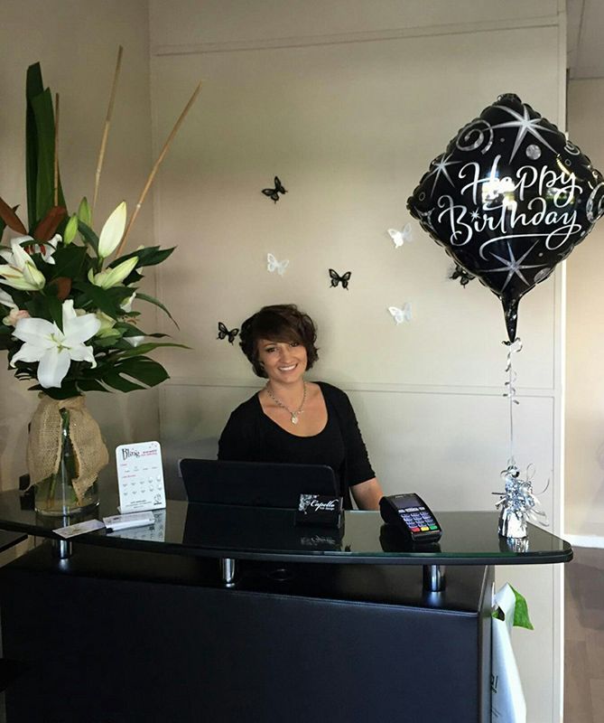 A Woman Is Sitting at A Desk in Front of A Happy Birthday Balloon — Capello Hair Design in Port Macquarie, NSW