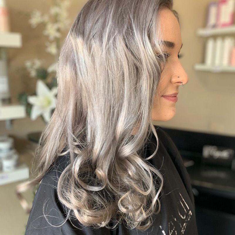 A Woman with Long Gray Hair Is Standing in A Salon — Capello Hair Design in Port Macquarie, NSW