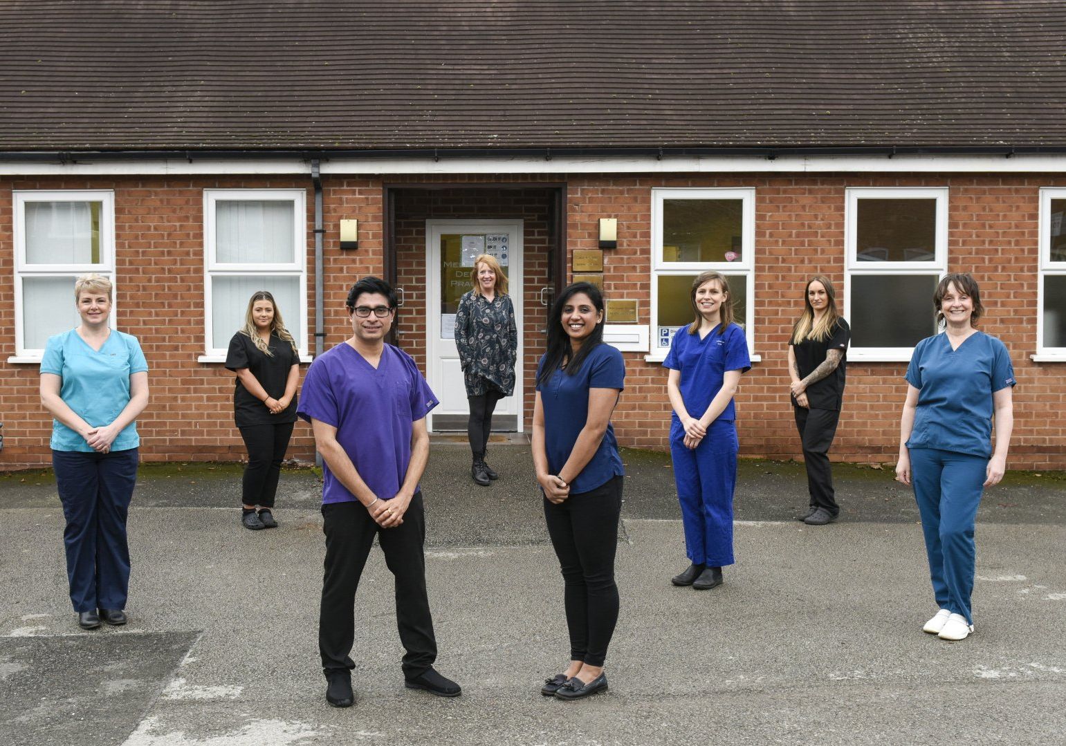 A group of nurses and doctors are standing in front of a brick building.