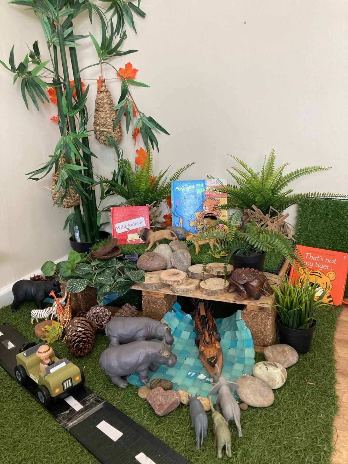 A toy car is driving down a road next to a table with animals and plants.