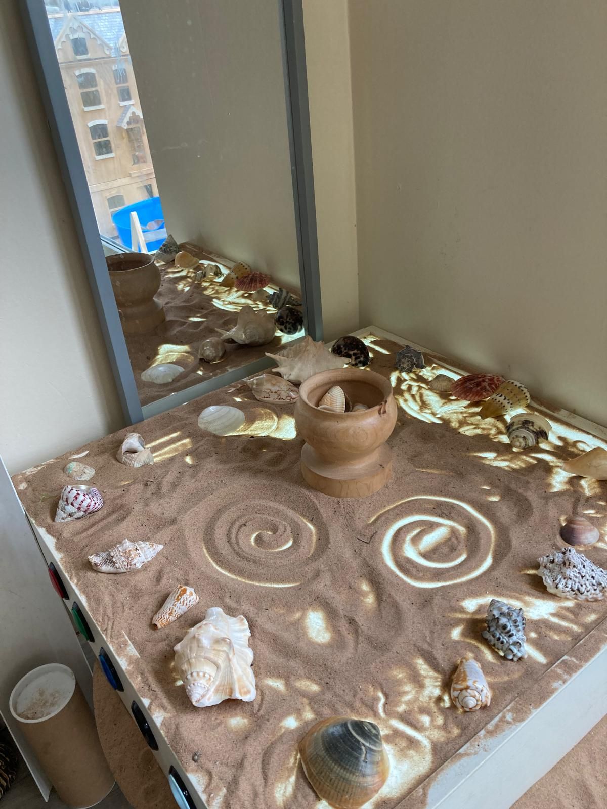 A table with sand and seashells on it in front of a mirror