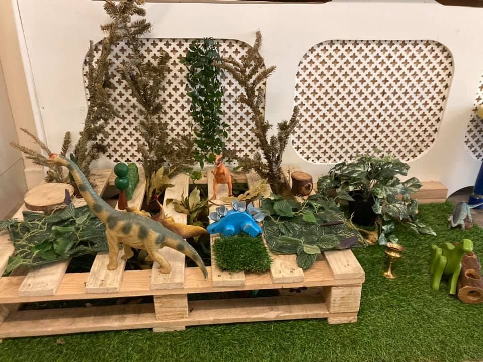 A wooden pallet filled with toy dinosaurs and plants.
