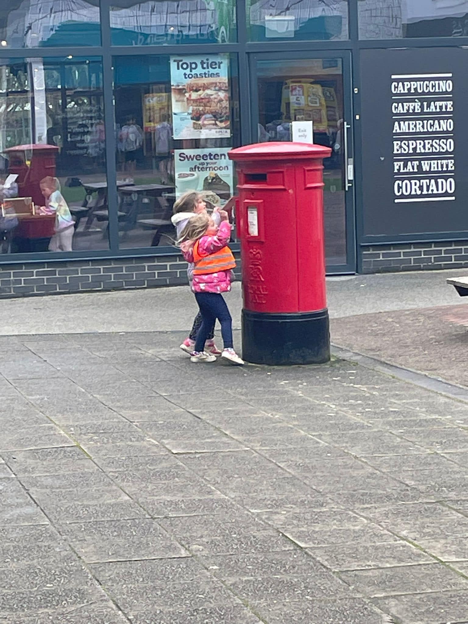 A couple of children standing next to a red mailbox.