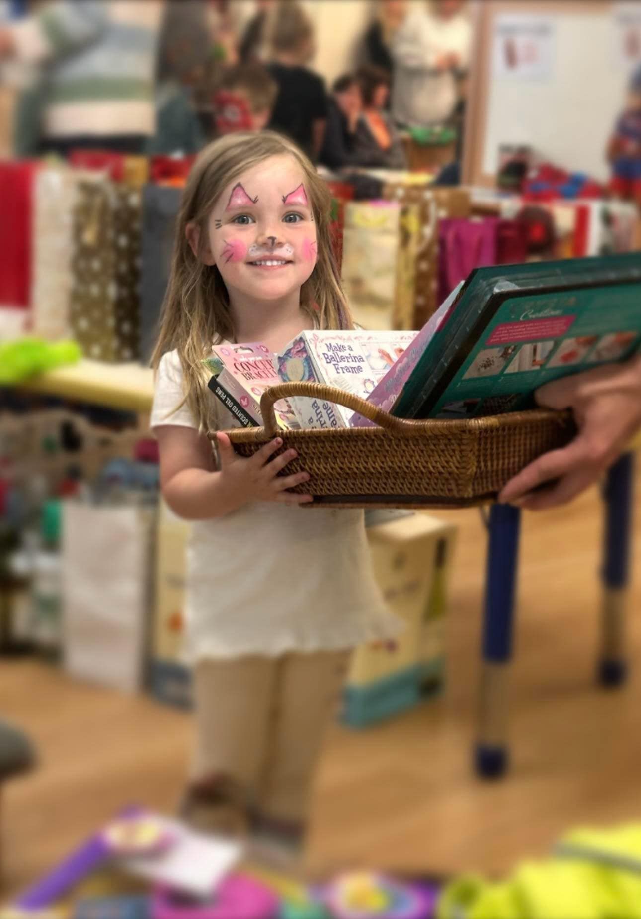 A little girl with face paint is holding a basket full of books