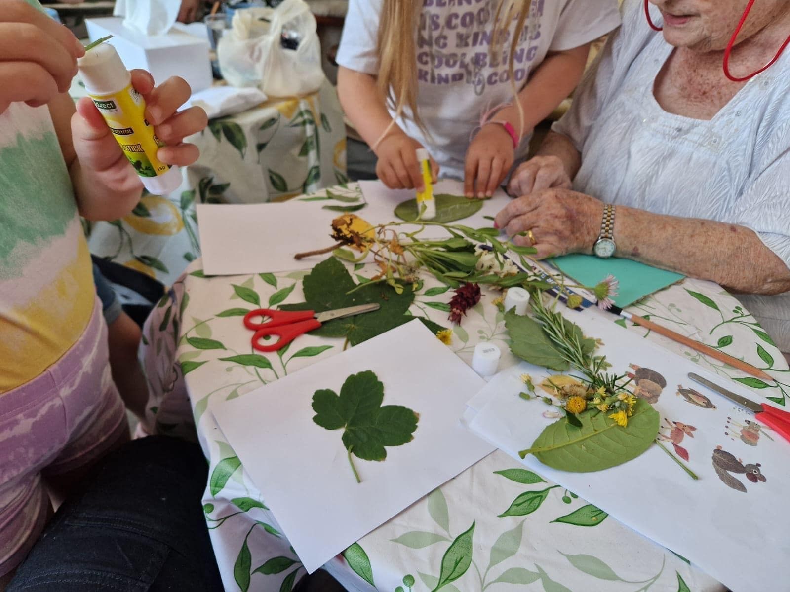 A group of people are sitting around a table with leaves and scissors