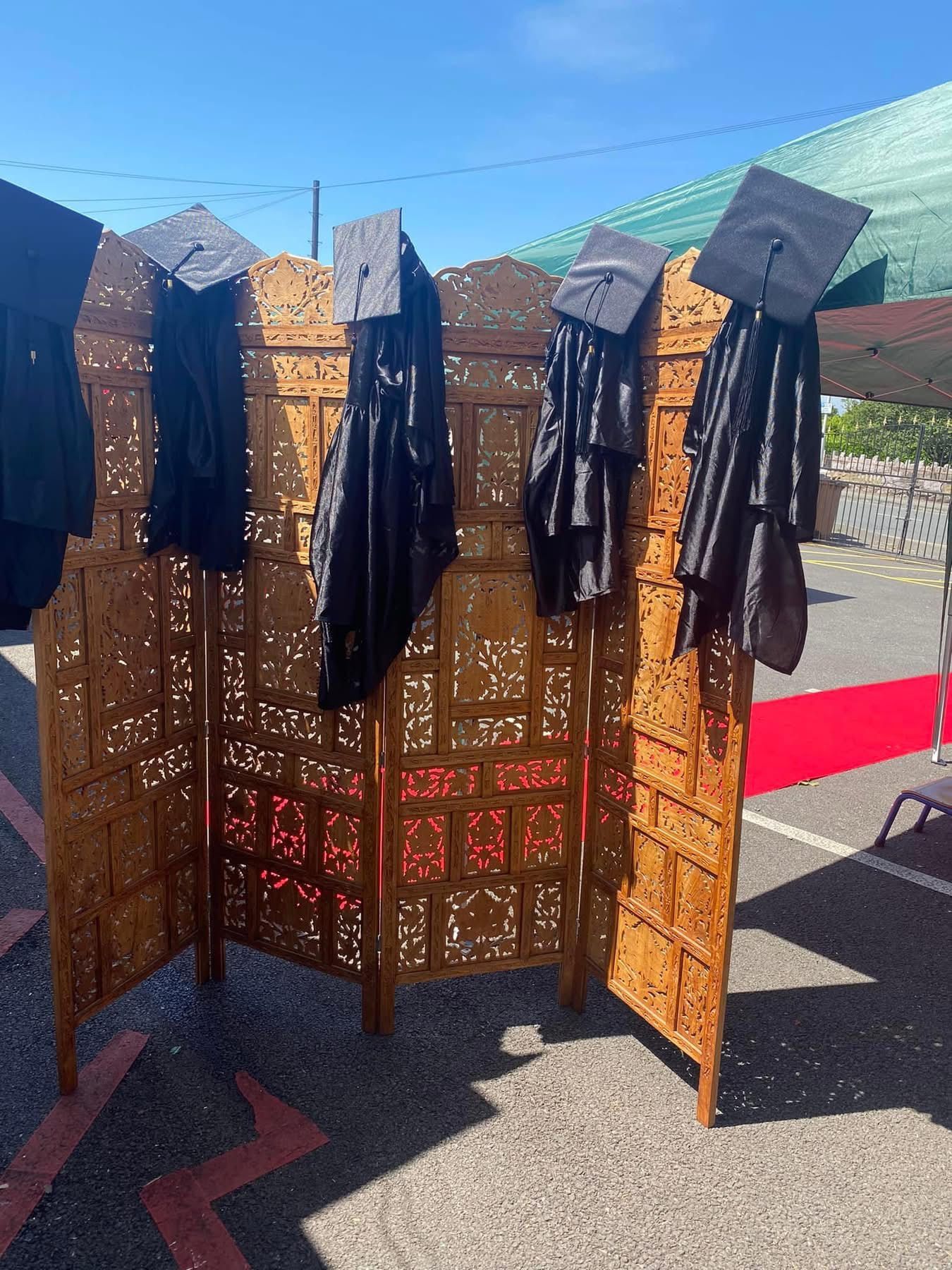 Graduation caps and gowns hanging on a wooden screen