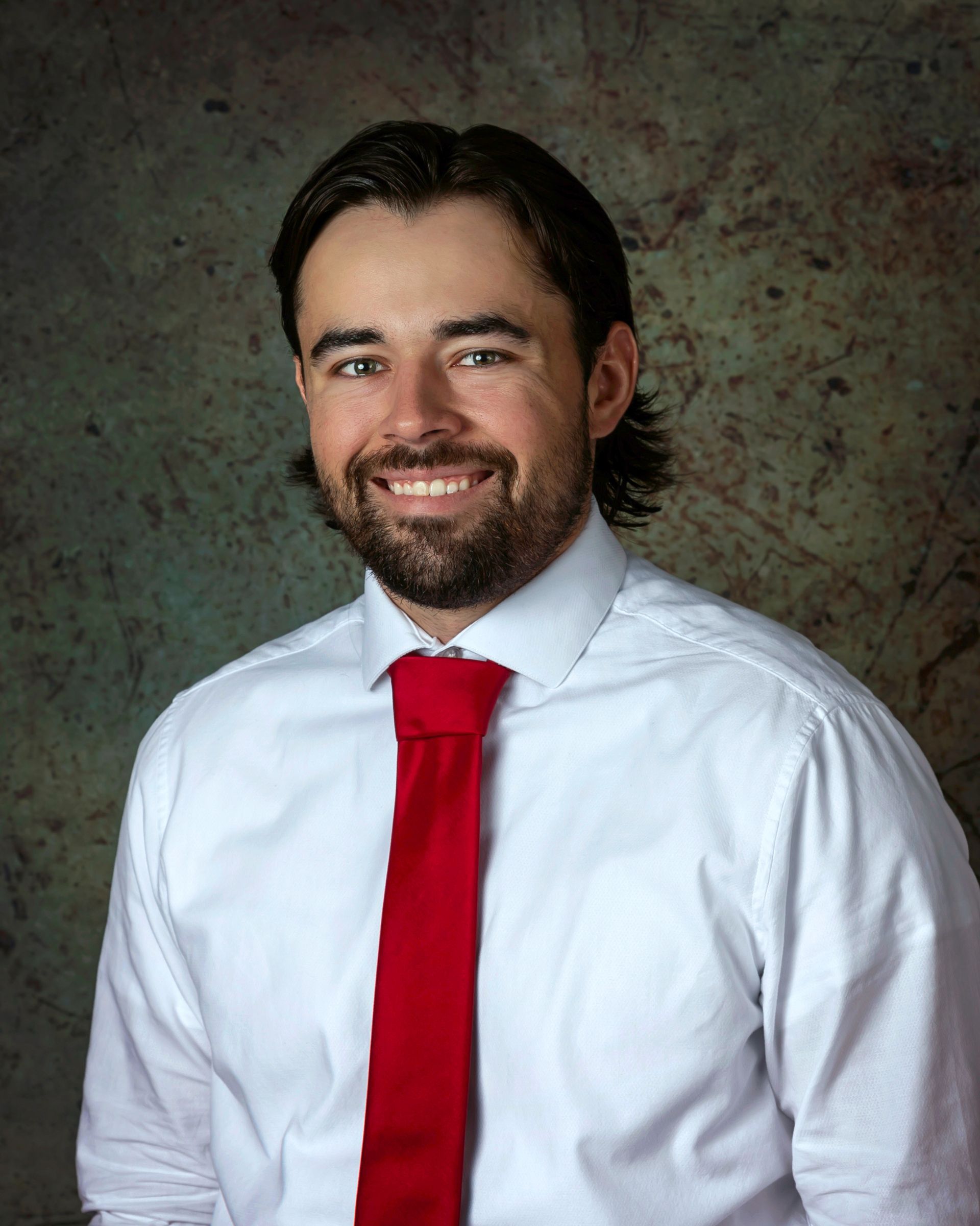 A man in a white shirt and red tie smiles for the camera