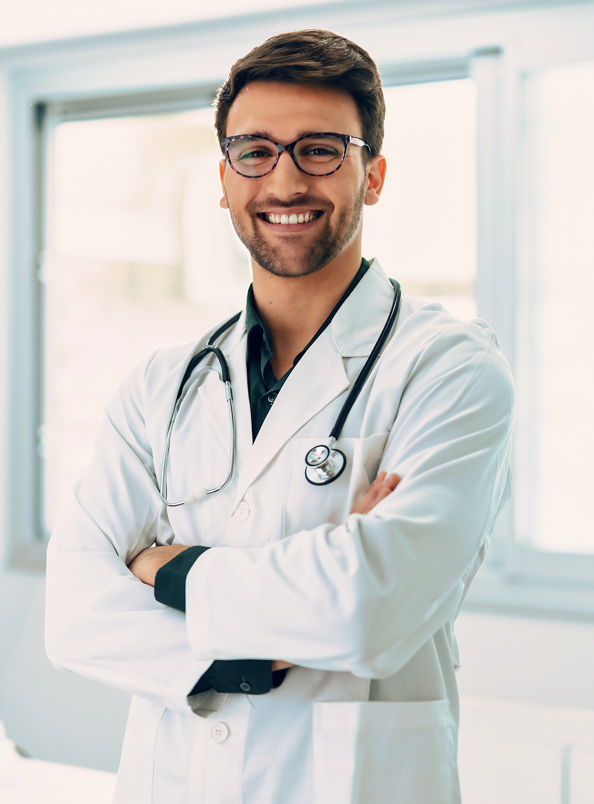 A doctor with a stethoscope around his neck is smiling with his arms crossed.