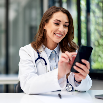 A female doctor is sitting at a table looking at her cell phone.