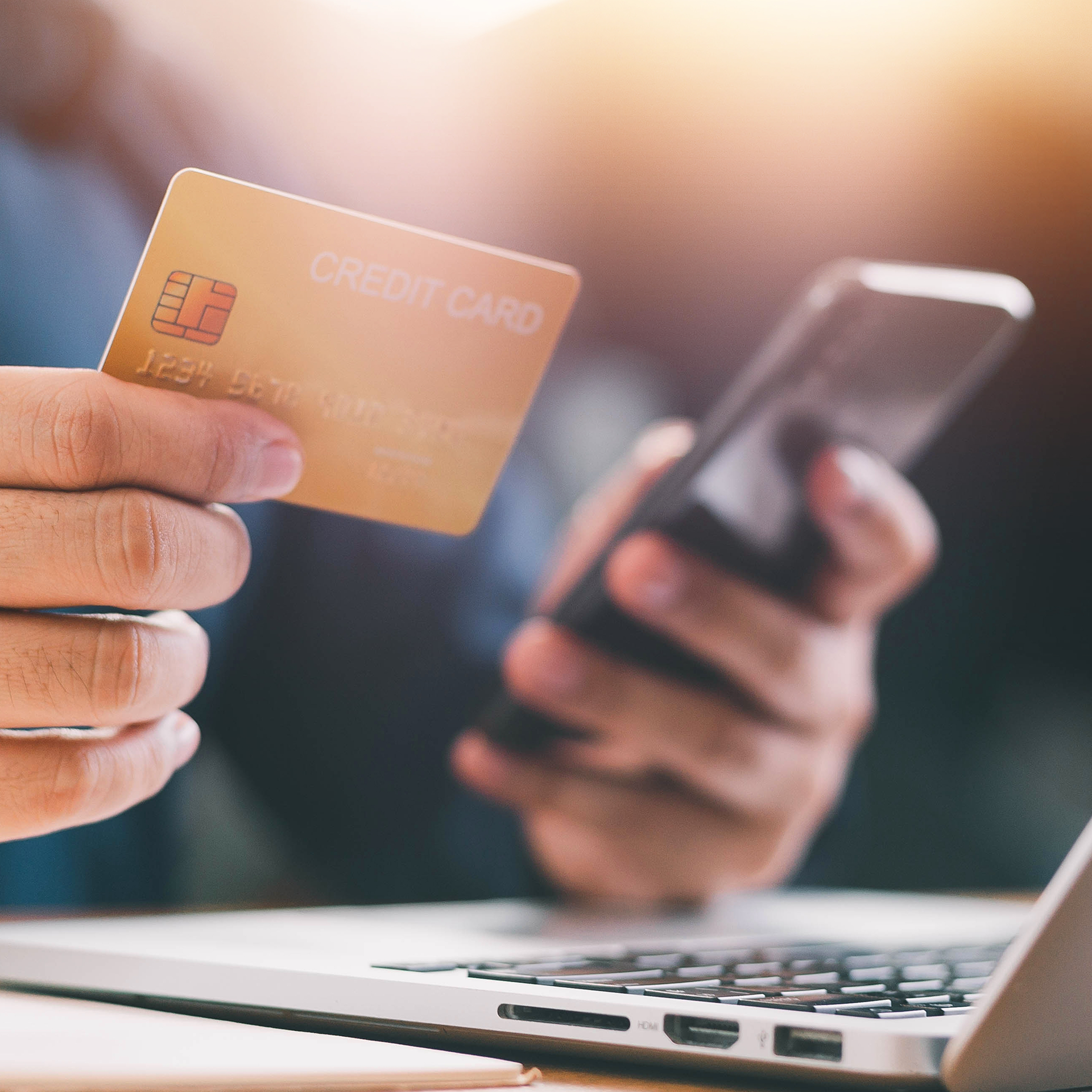 A person is holding a credit card and a cell phone in front of a laptop.