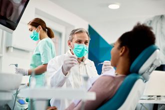 A dentist wearing a mask is examining a patient 's teeth in a dental office.