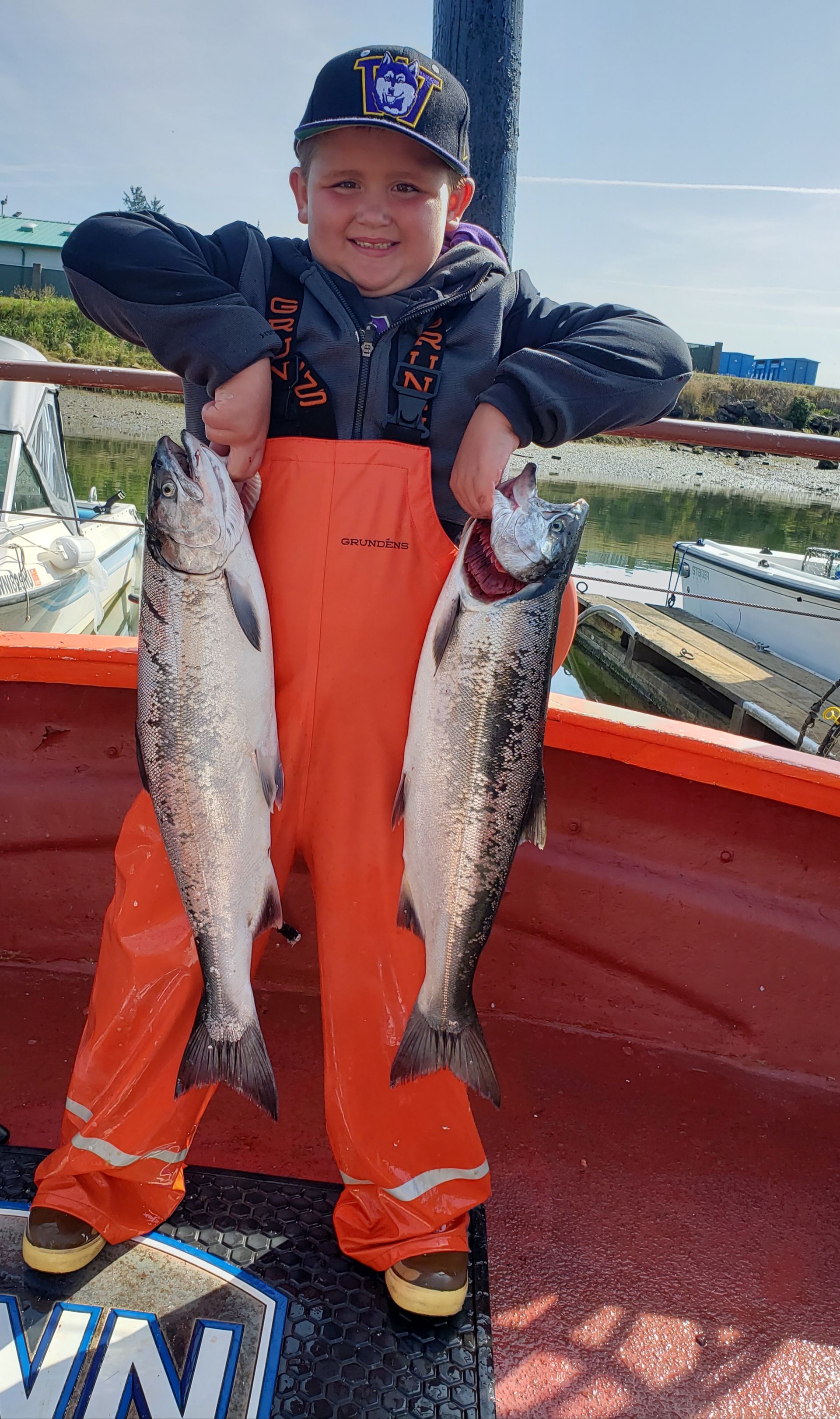 A young boy is holding two fish in his hands on a boat.