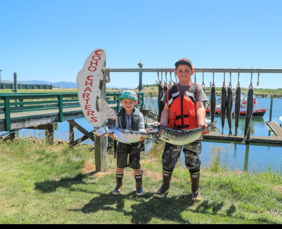 Two boys holding fish in front of a sign that says coho charters
