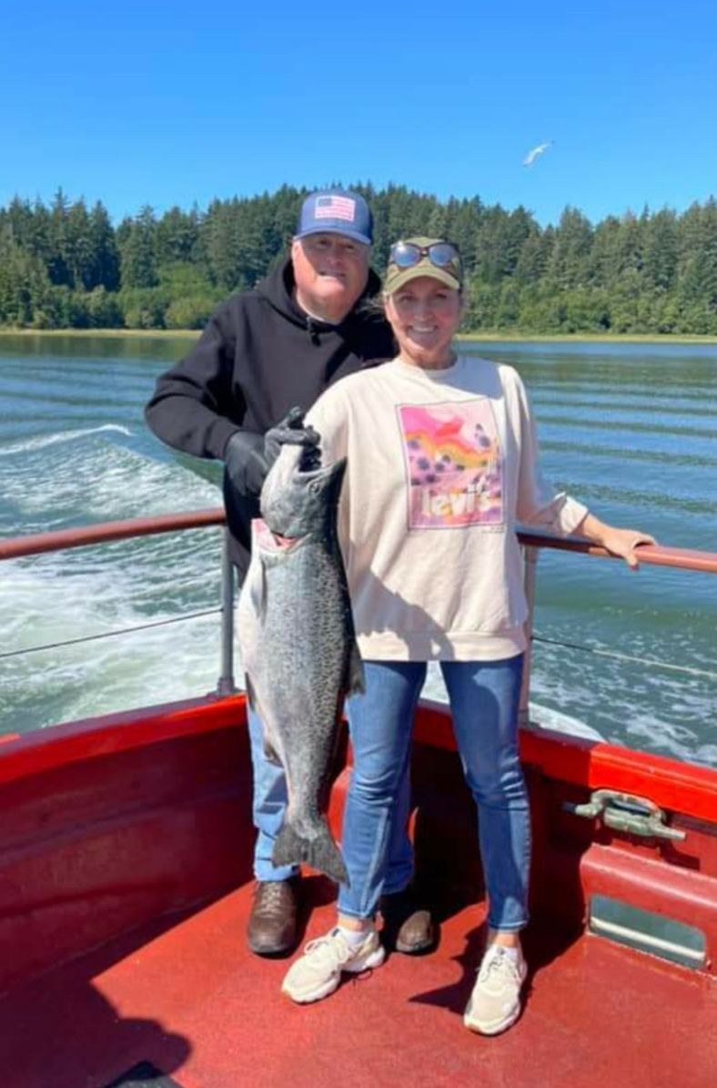 A man and a woman are standing on a boat holding a large fish.