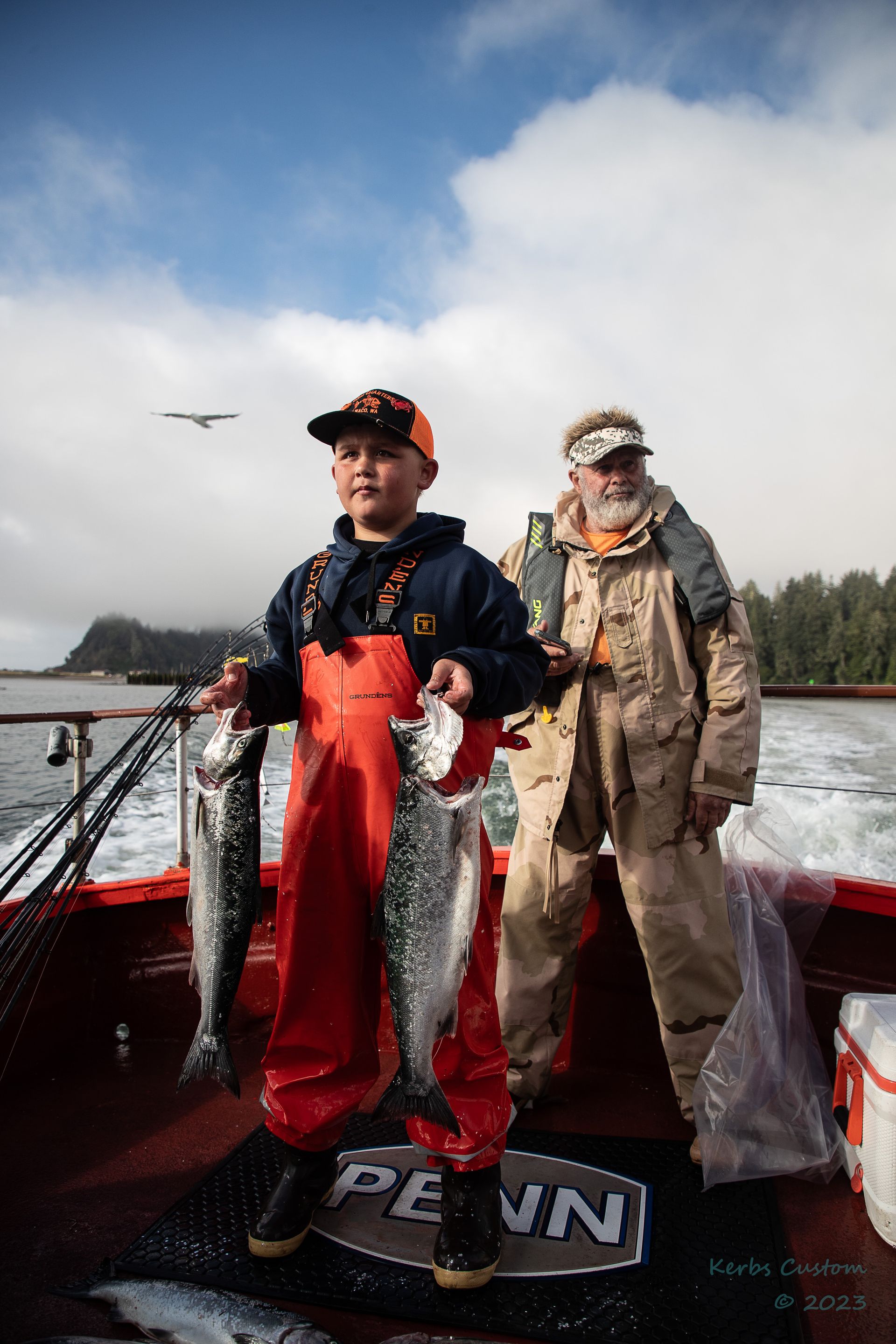 A man and a boy are standing on a boat holding fish.