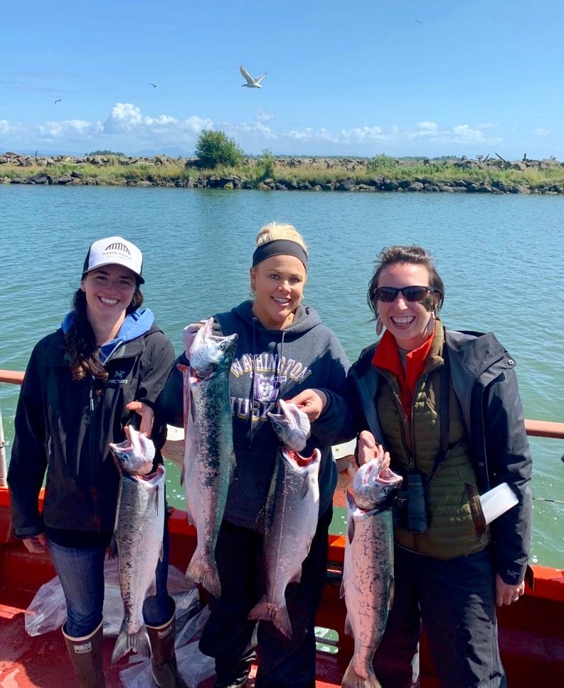 Three people are standing on a boat holding fish.