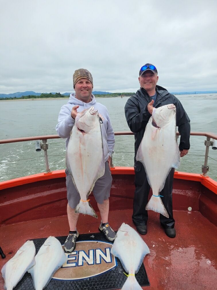 Two men are standing on a boat holding large fish.