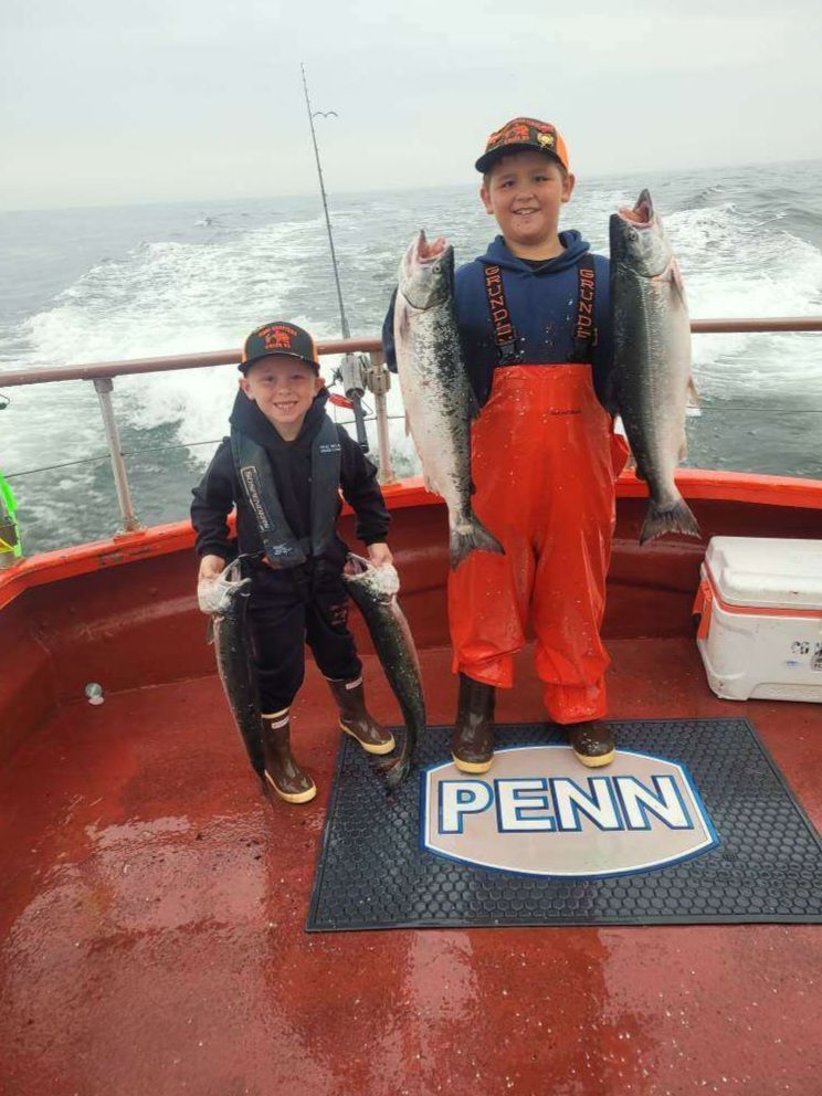 Two young boys are standing on a boat holding fish.