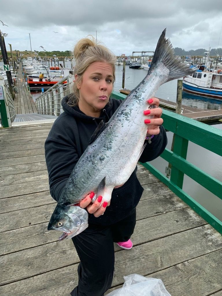 A woman is holding a large fish on a dock.