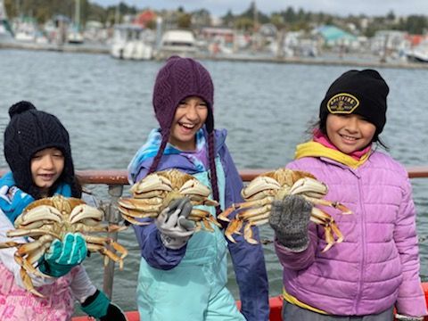 Three young girls are holding crabs on a boat.